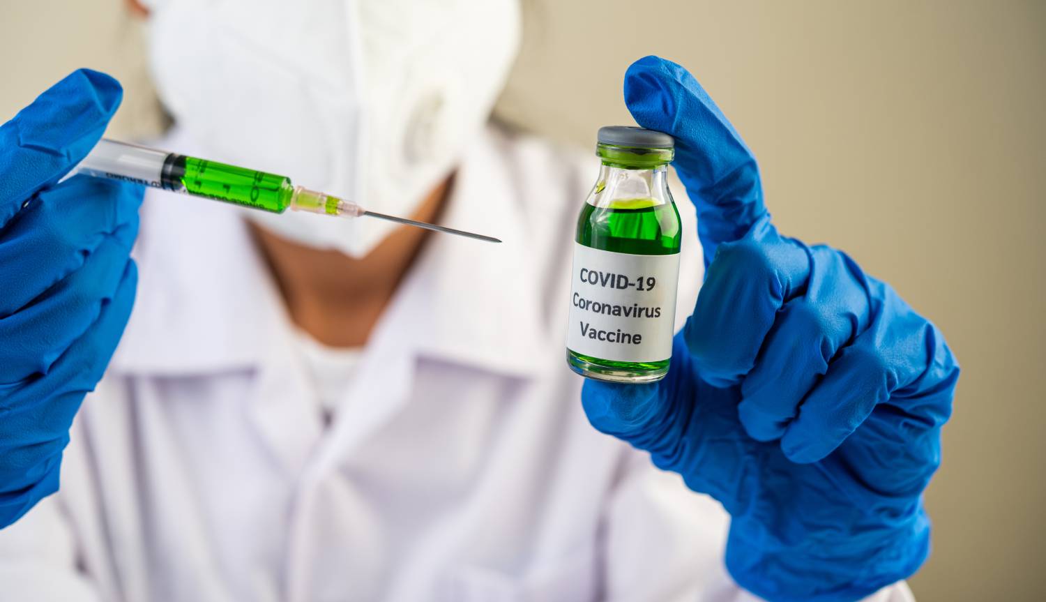 Scientists wearing masks and gloves holding a syringe with a vaccine to prevent covid 19 1